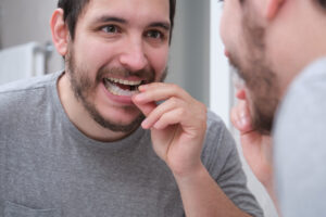 Young latin man wearing orthodontic silicone trainer or invisible braces aligner. Mobile orthodontic appliance for dental correction.