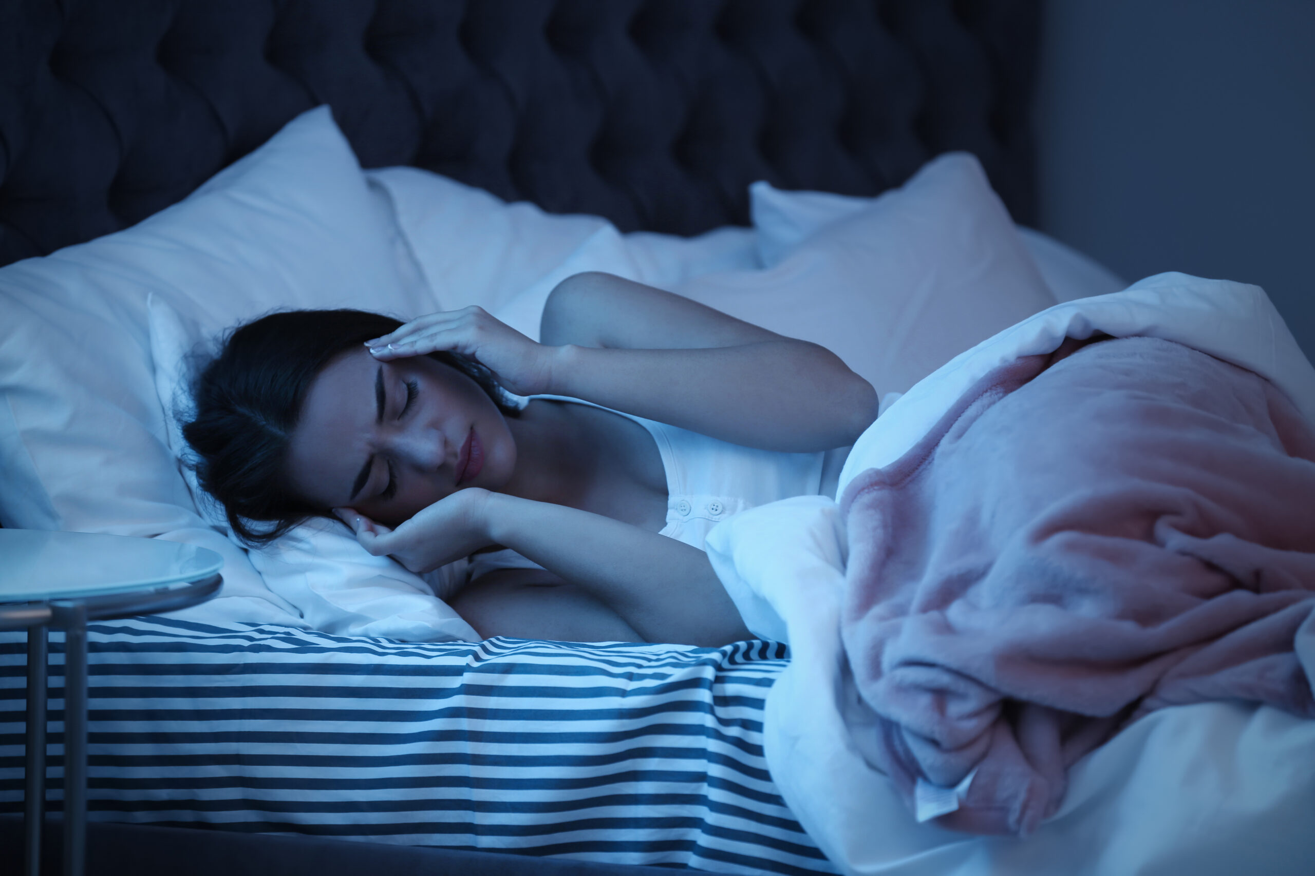 Young woman suffering from headache while lying in bed at night. Sleeping problems