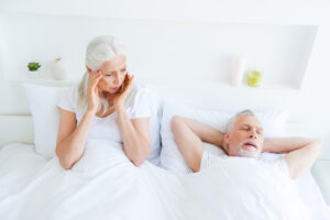 Relax, rest, retired, concept. I'm very tired! Gray hair woman looks aside, holder ears and close eyes siting on the bed linen, sheets and look on daydream sleeping husband