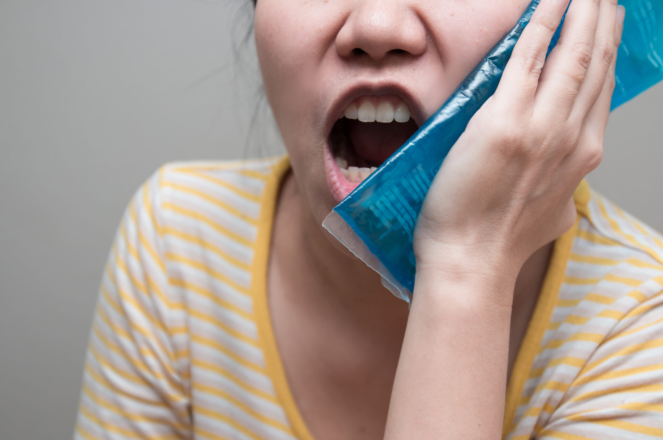 Asian woman suffering from toothache and using cold pack jelly. Concept of teeth problem.